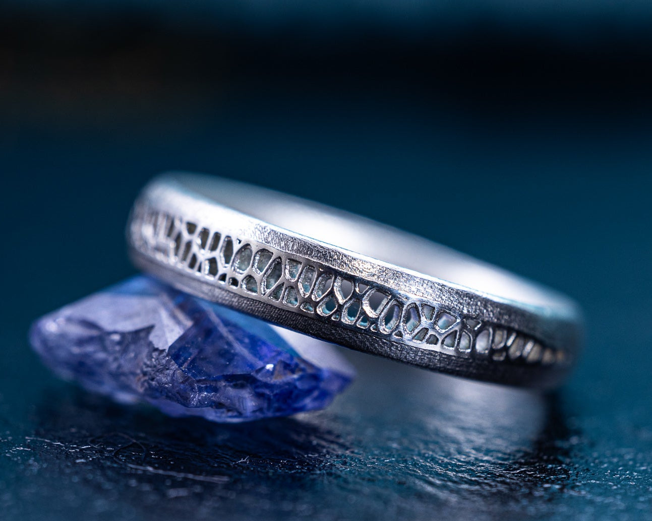 Silver ring with intricate design on a reflective blue surface