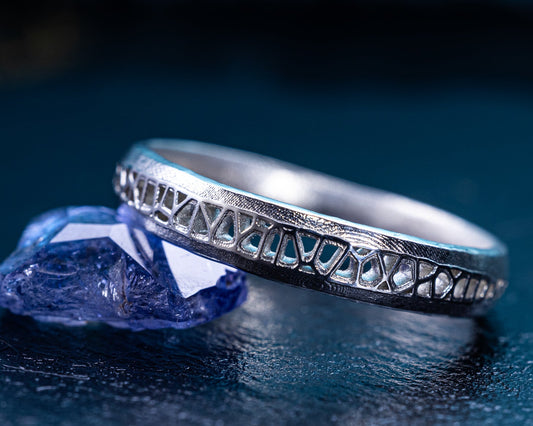 Silver ring with intricate design on a dark blue background