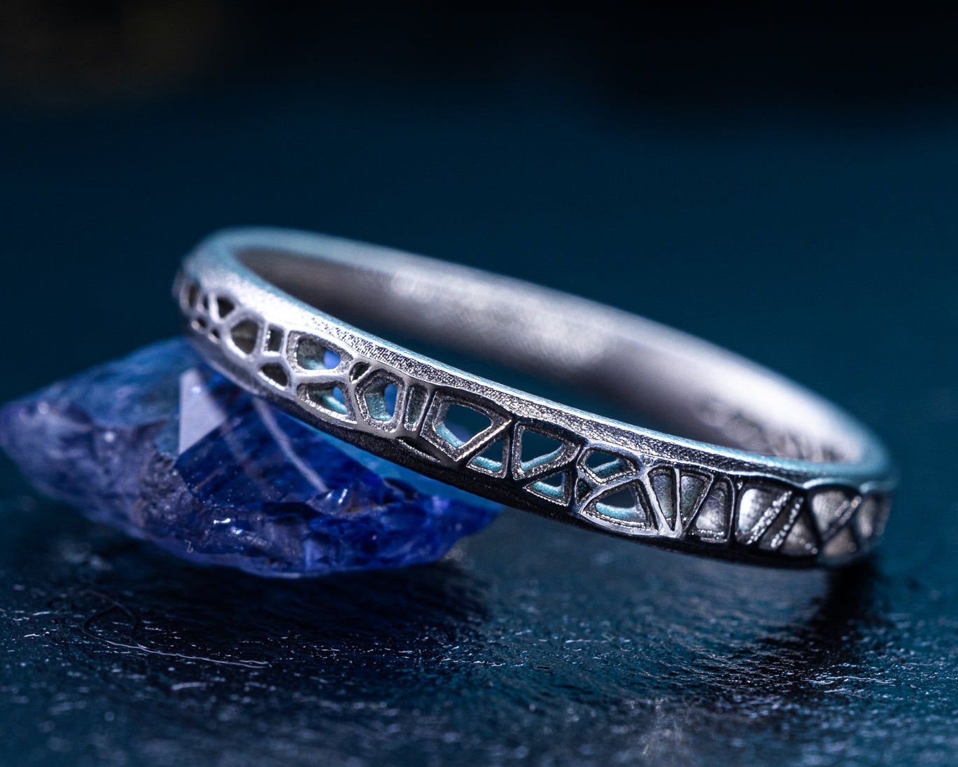 Silver ring with intricate design on a dark blue background