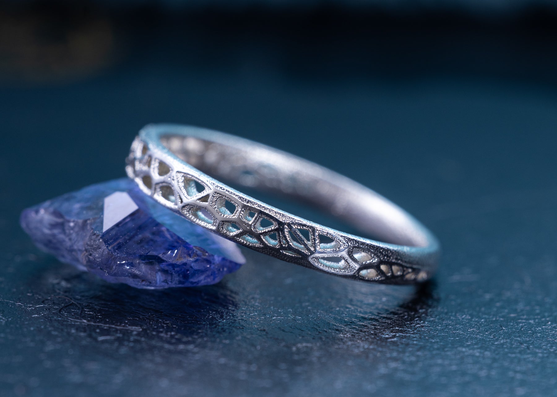 Silver ring with intricate design on a dark blue background
