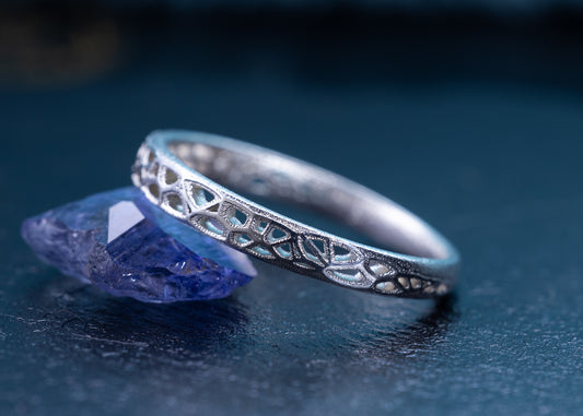 Silver ring with intricate design on a dark blue background